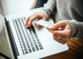 Woman looks at credit card while working on computer to check accounts