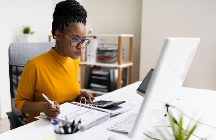 Propietaria de una empresa sentada frente a una computadora, manteniendo registros de contabilidad de su negocio